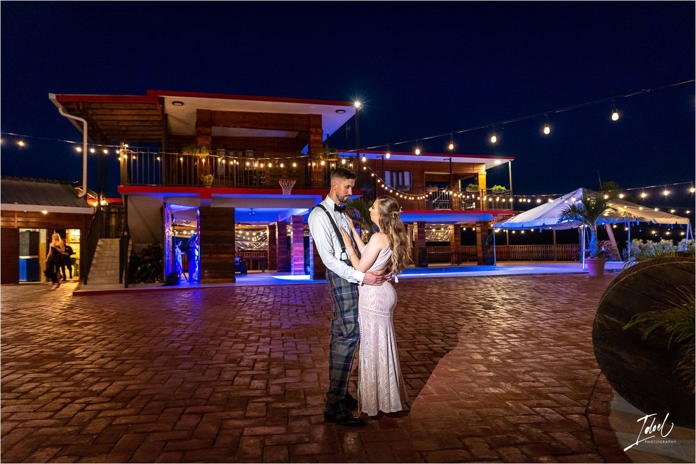 Night portrait at waterfront venue with blue lighting and brick paved pathway.