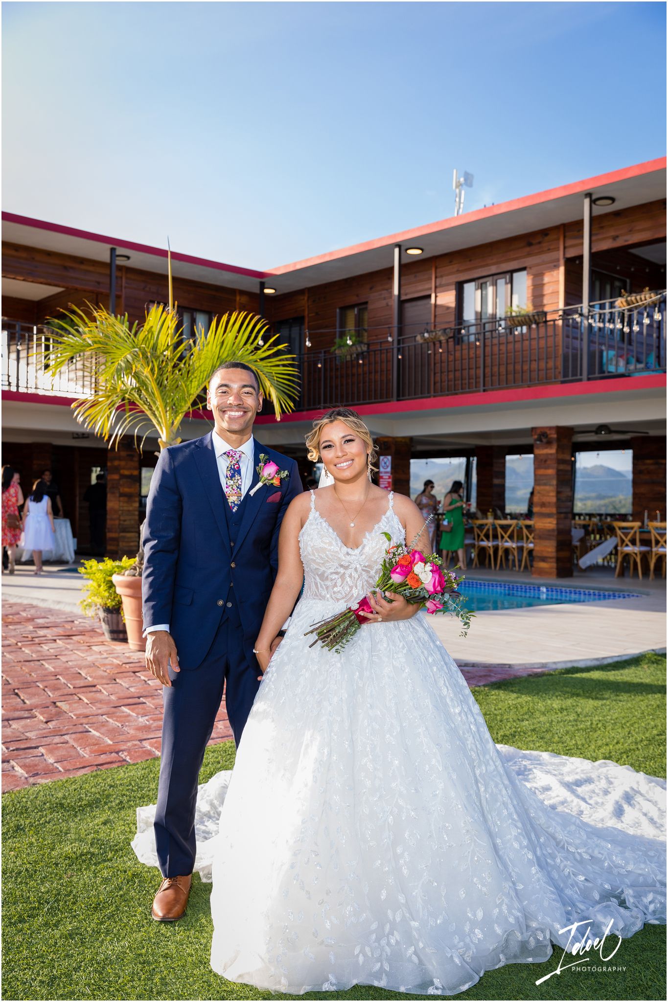 Elegant outdoor wedding portrait at venue with Spanish-style architecture and palm trees.