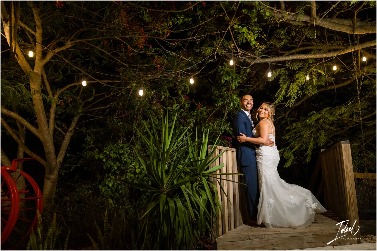 Evening wedding portrait on a garden deck with string lights and tropical plants.