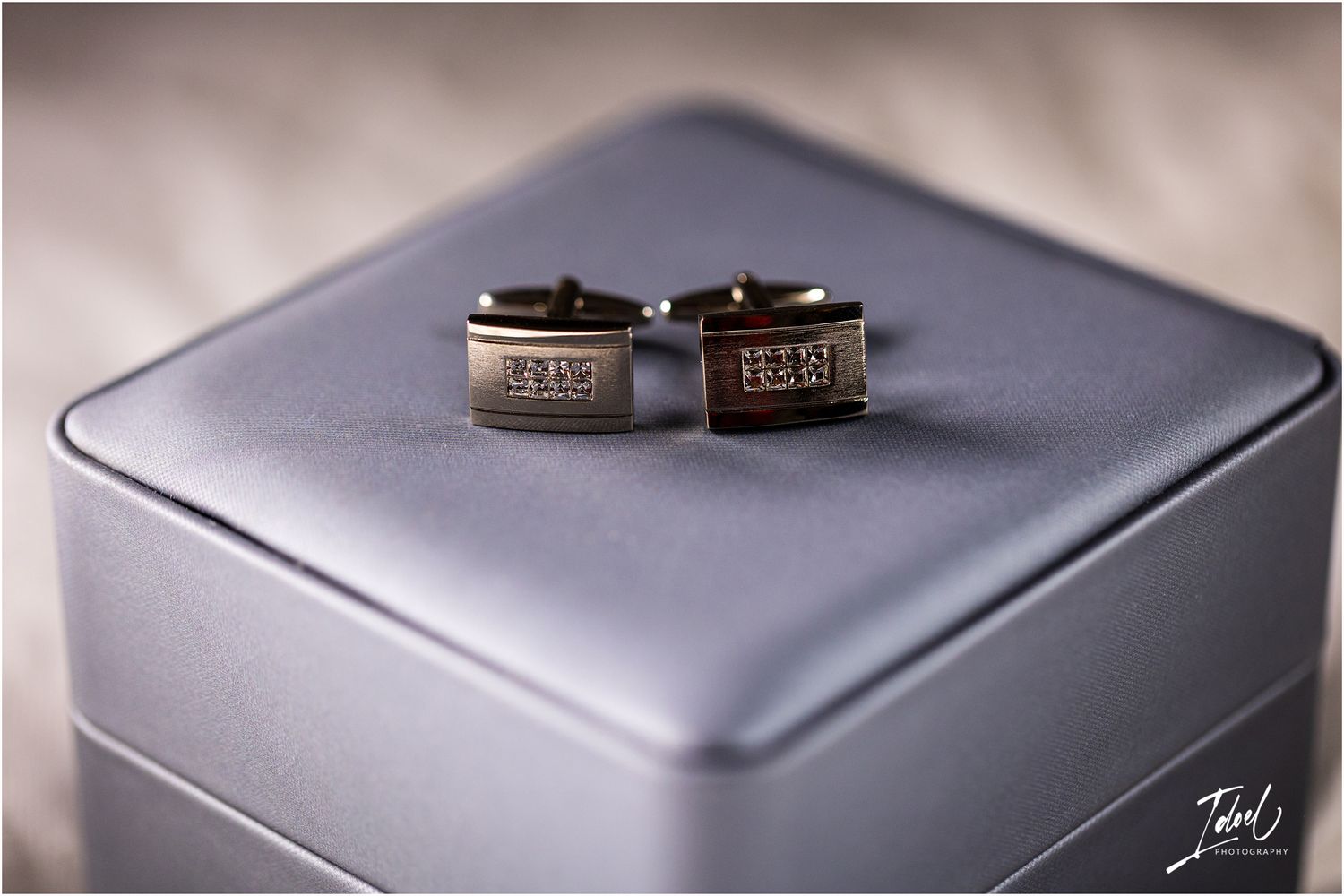 Silver metallic cufflinks displayed on a modern square jewelry box.