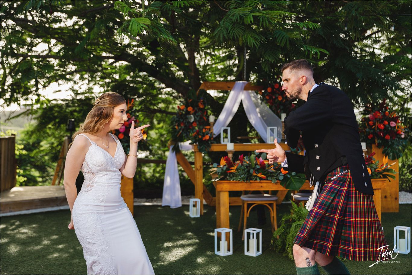 Celebratory dance moment at outdoor wedding with decorated wooden arch and lanterns in background.