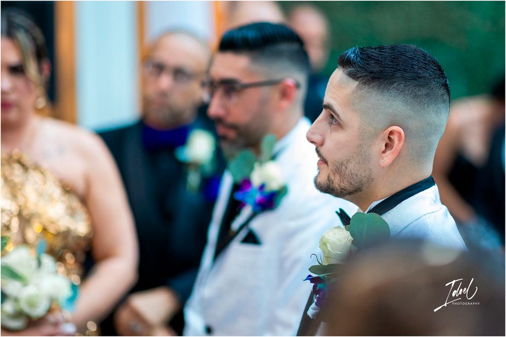 Wedding guests looking on during ceremony with soft focus green background and decorative boutonnieres.