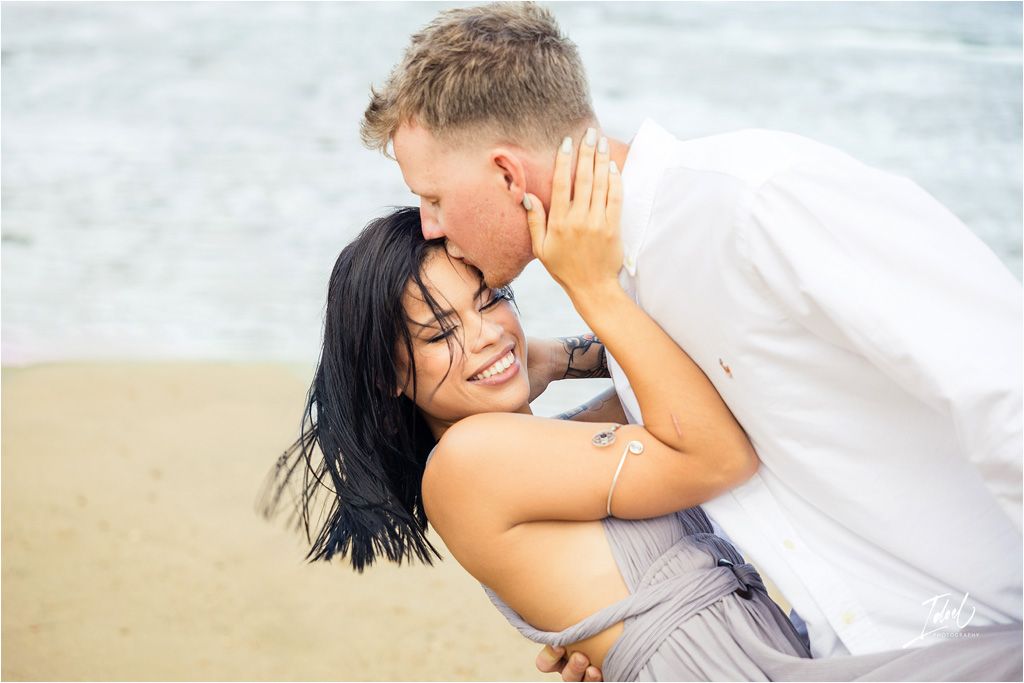 Romantic beach moment captured with dramatic ocean backdrop.