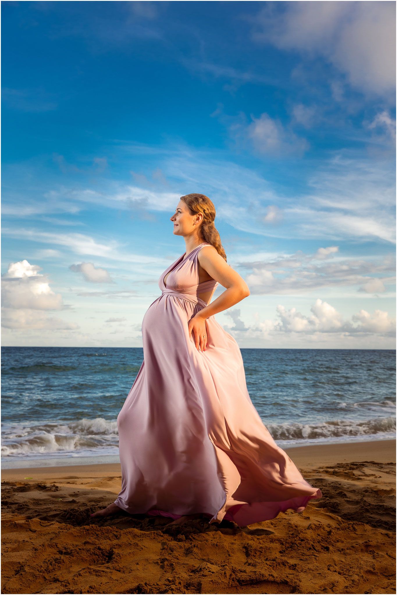 Mauve dress flows in wind during oceanside maternity photoshoot.