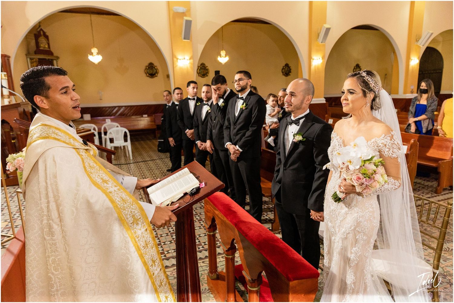 A Catholic wedding ceremony with priest, wedding party, and guests gathered at the altar.
