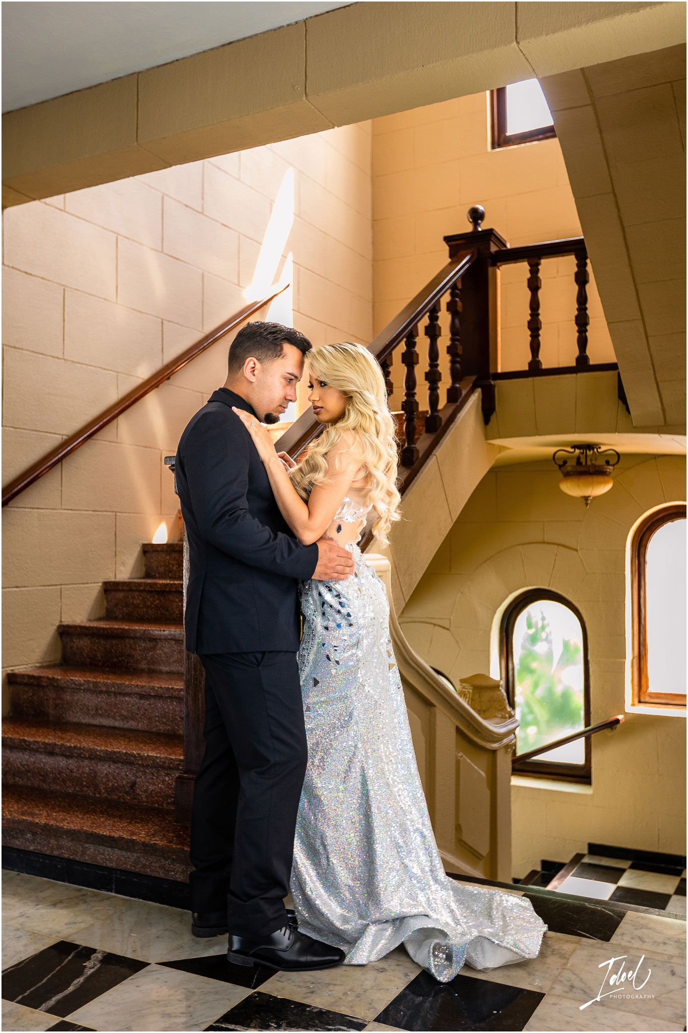 Elegant couple embraces on vintage staircase in historic building with arched windows.