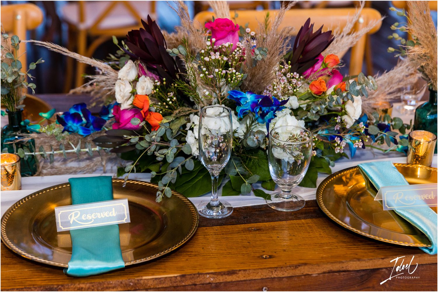 Elegant table setting with vibrant floral centerpiece, gold charger plates, and turquoise napkins.
