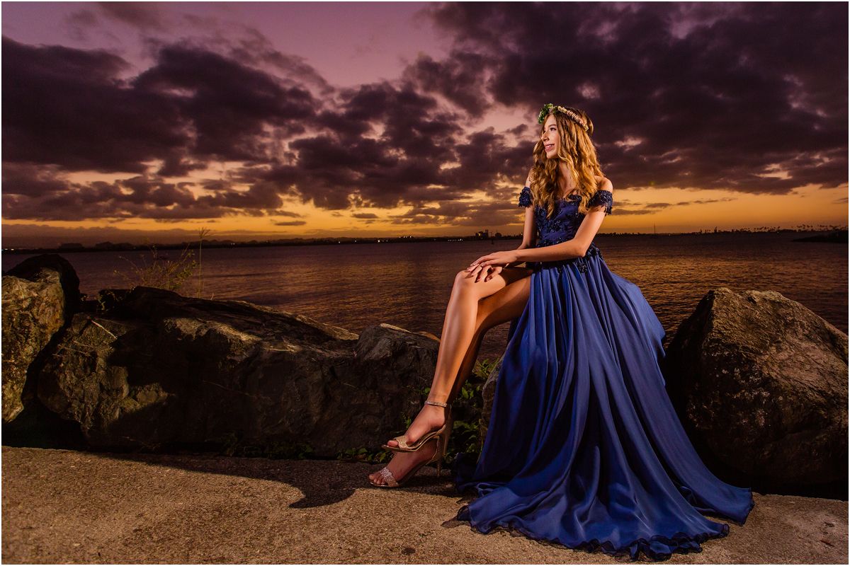 A person in a flowing blue dress stands at the edge of the Grand Canyon during a dramatic sunset.