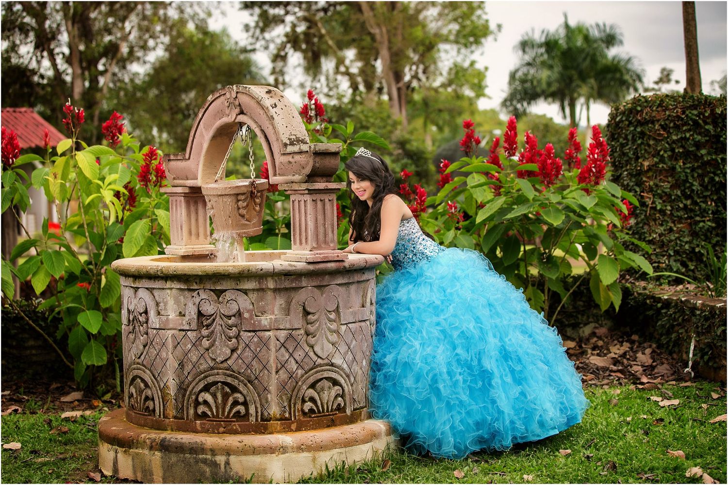 Quinceañera photo session with blue ballgown dress in garden setting with stone columns.