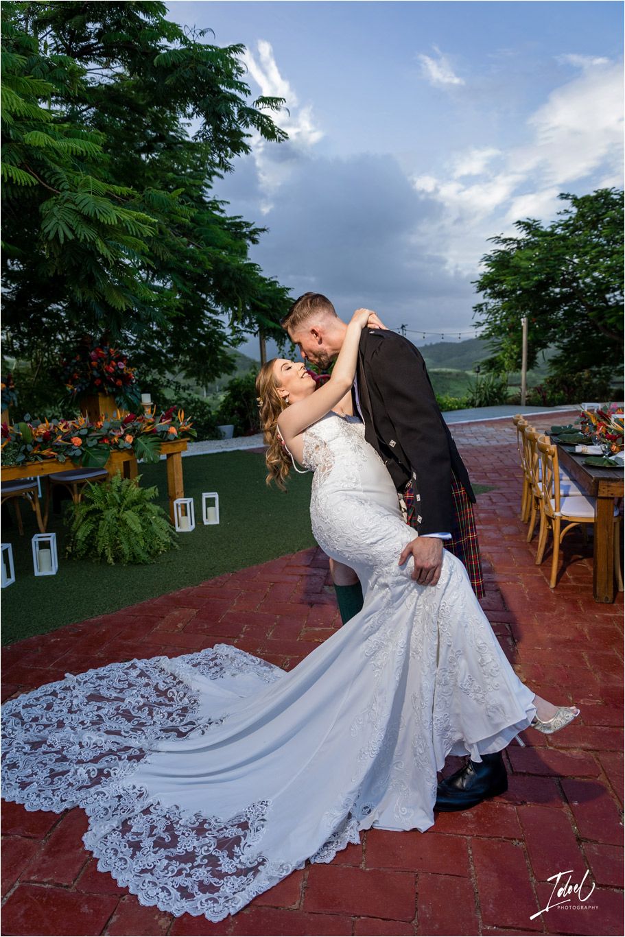 A romantic dip pose on a brick patio with a flowing lace wedding dress train.