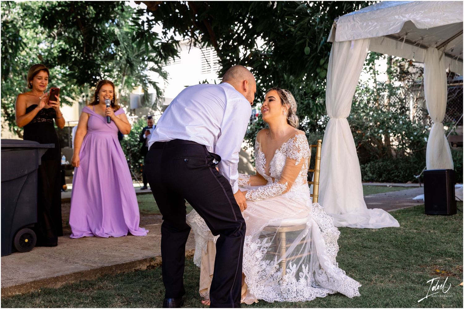 Outdoor wedding ceremony moment with guests in purple dresses watching nearby.