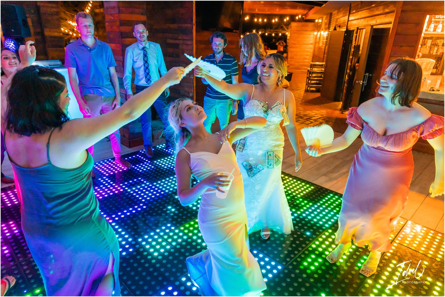 Wedding guests dancing on a colorful LED dance floor illuminated with rainbow lights.