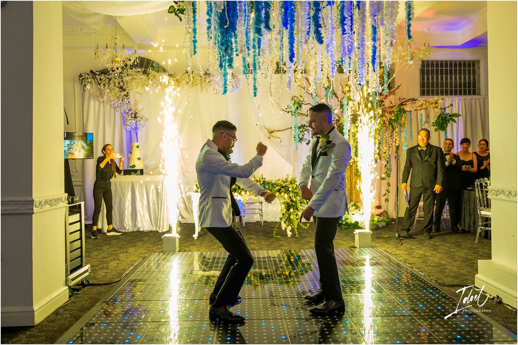 Two people dance together under a decorative ceiling with flowing blue and white streamers at an elegant indoor event.