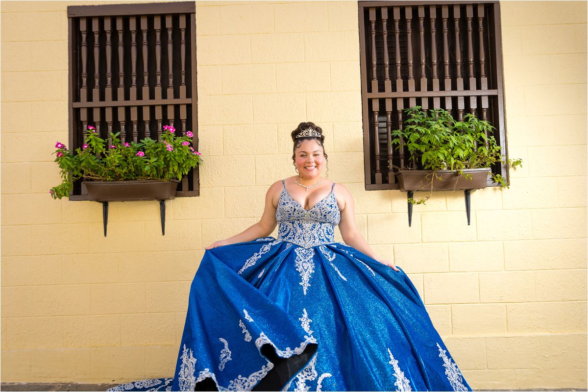 A blue quinceañera dress with silver embellishments and a full skirt is photographed in multiple angles against a beige wall.