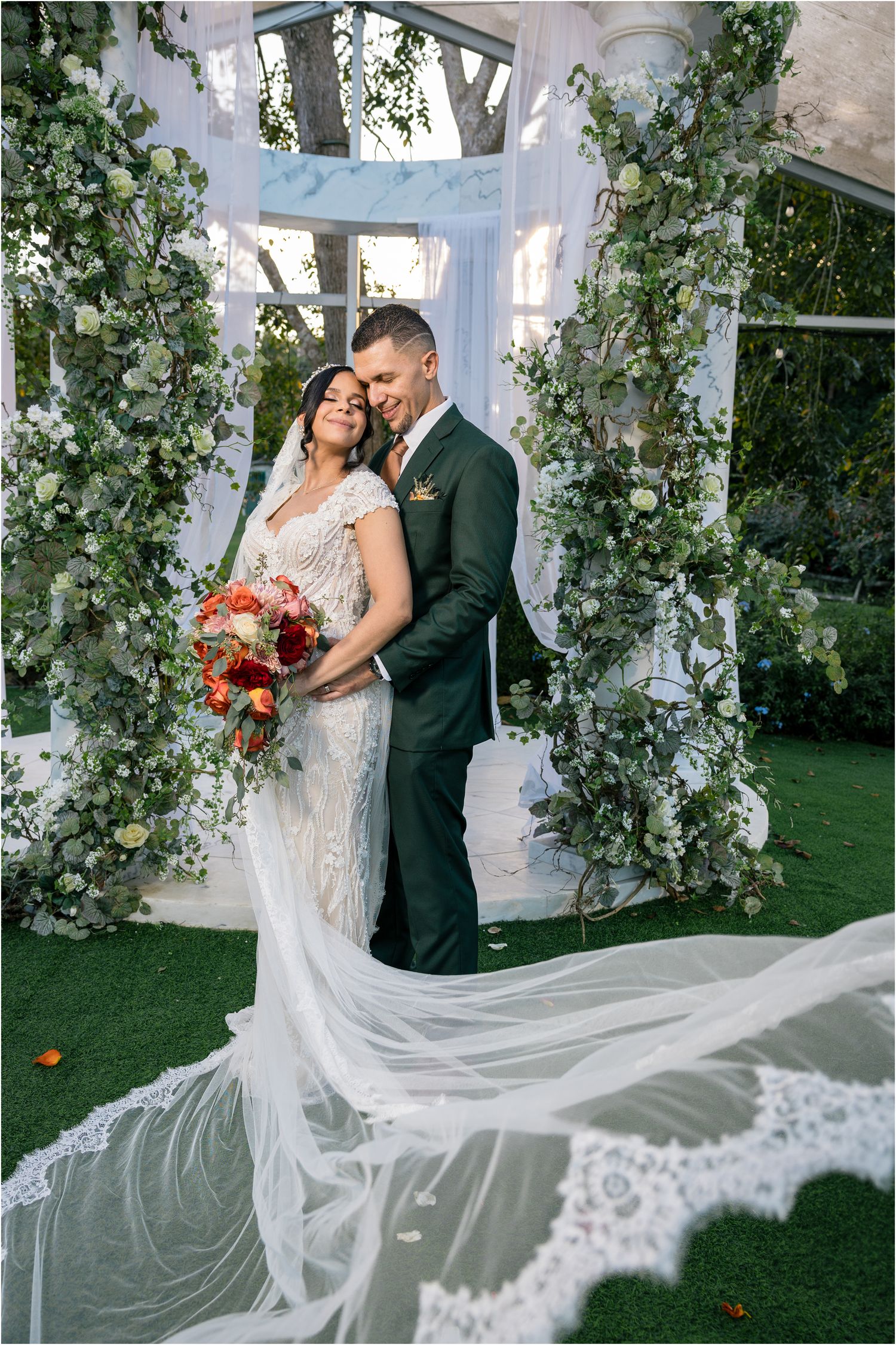 A romantic wedding ceremony under a floral arch with greenery and flowing white dress train.