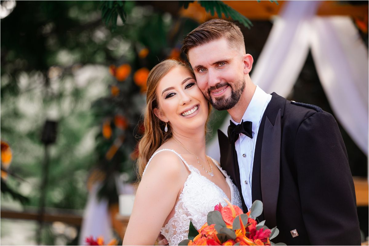 Newlywed couple shares romantic moments in a garden setting with vibrant orange floral accents.