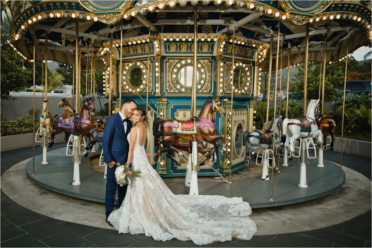 Bride and groom share a romantic kiss in front of a vintage carousel at their wedding venue.