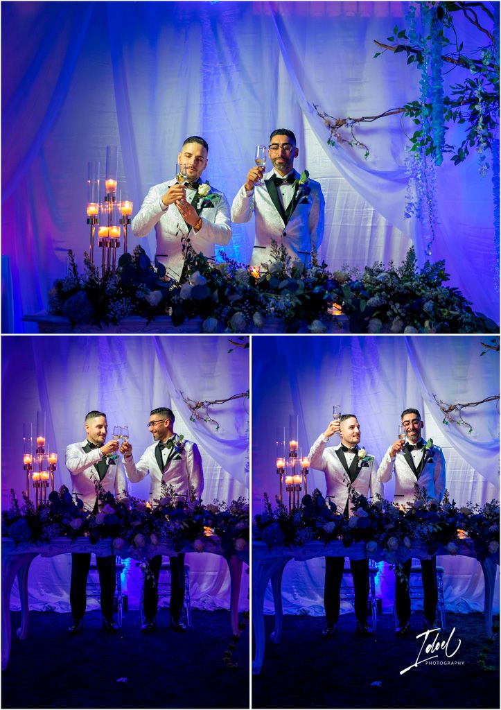Wedding couple poses together with drinks at elegant reception with dramatic blue lighting and floral decor.