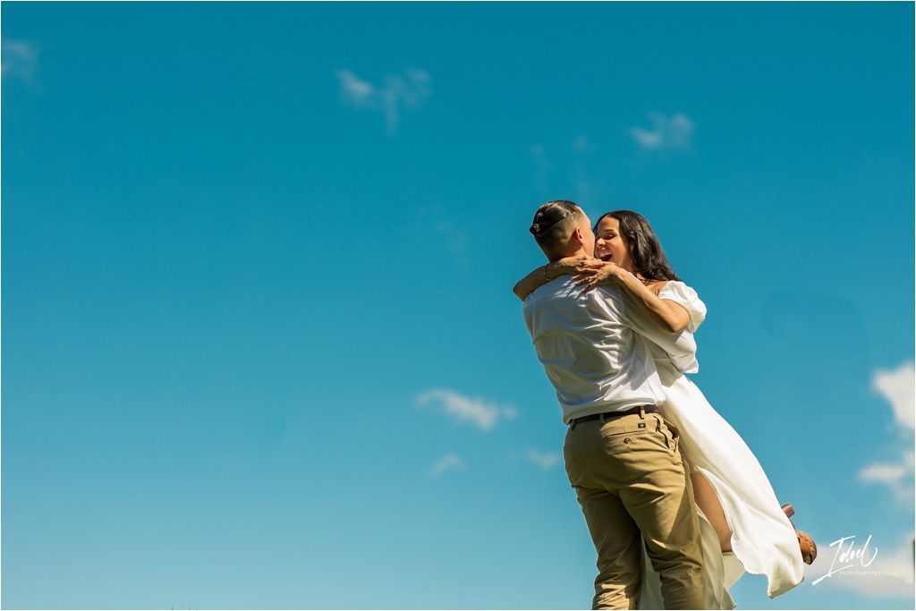 A couple embraces against a bright turquoise sky on a sunny summer day.