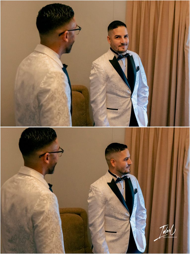 Reflection of a groom in a white jacket and bow tie looking at himself in a mirror with elegant curtains in the background.
