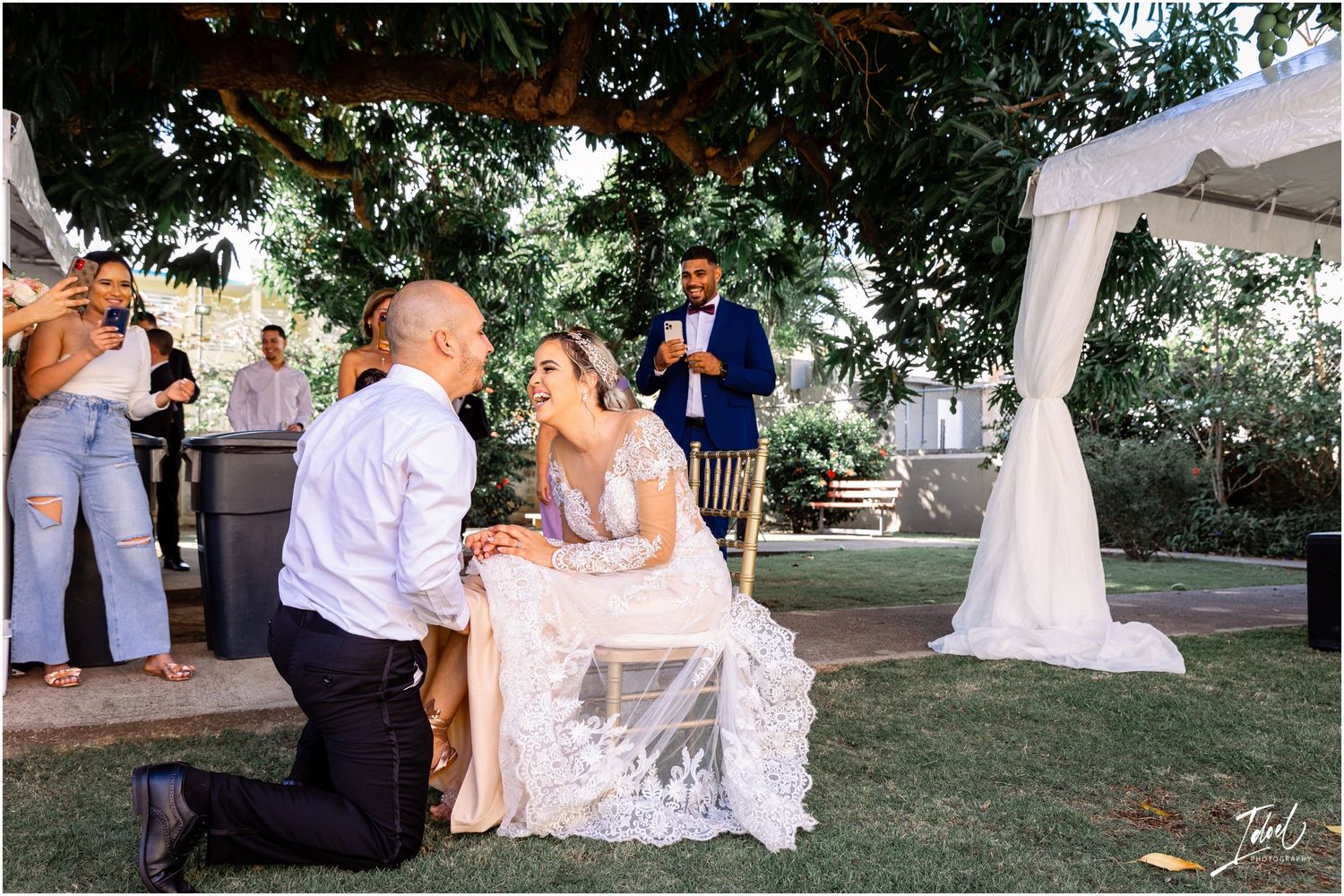 Wedding celebration scene on grass lawn with white tent and guests watching.