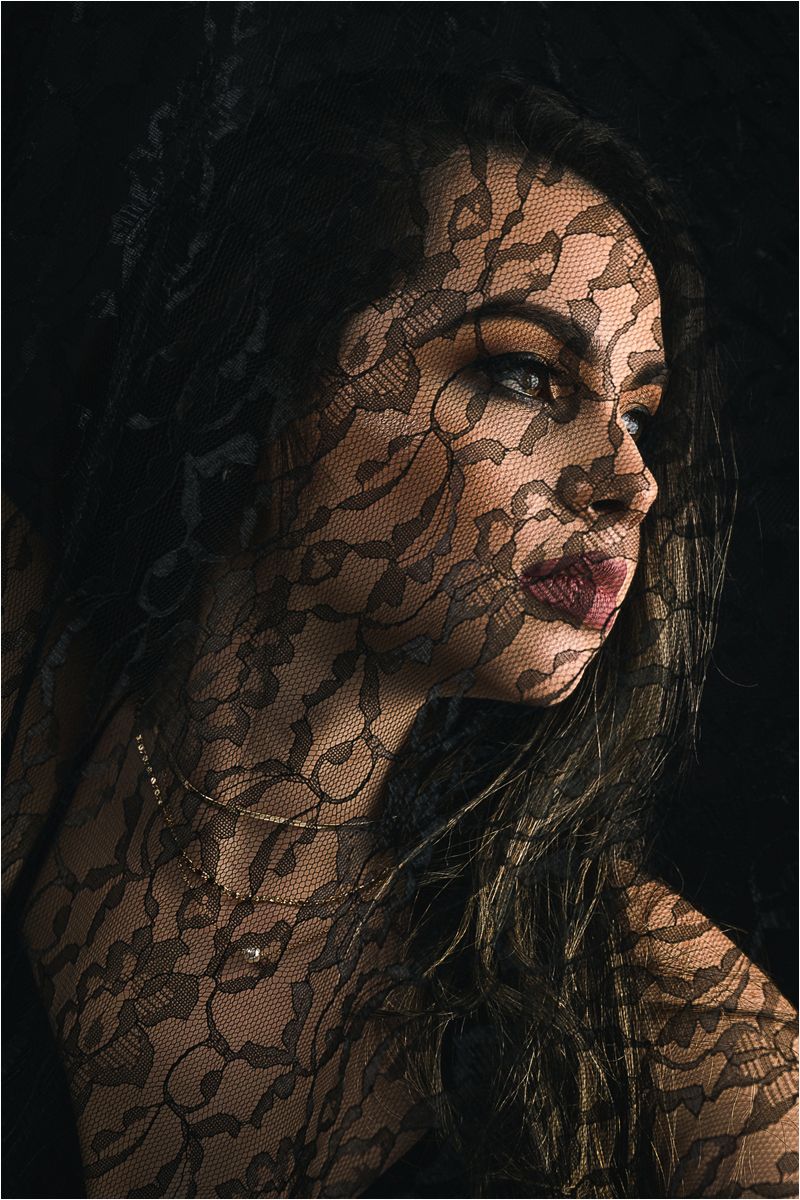 Artistic portrait with intricate black lace pattern shadows creating a dramatic and moody effect on skin and features.
