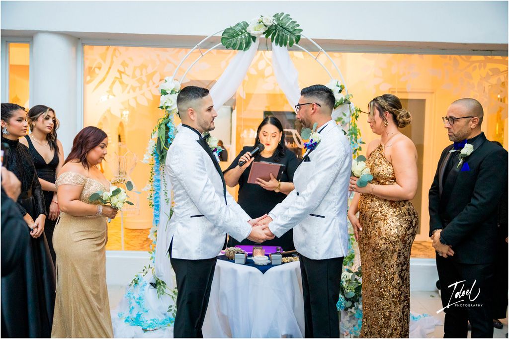 An elegant wedding ceremony takes place under a floral arch with guests gathered to witness the special moment.