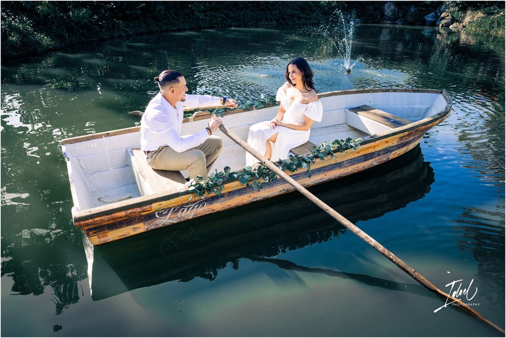 A romantic scene with couple on a wooden rowboat decorated with flowers in a tranquil pond with reflective water.