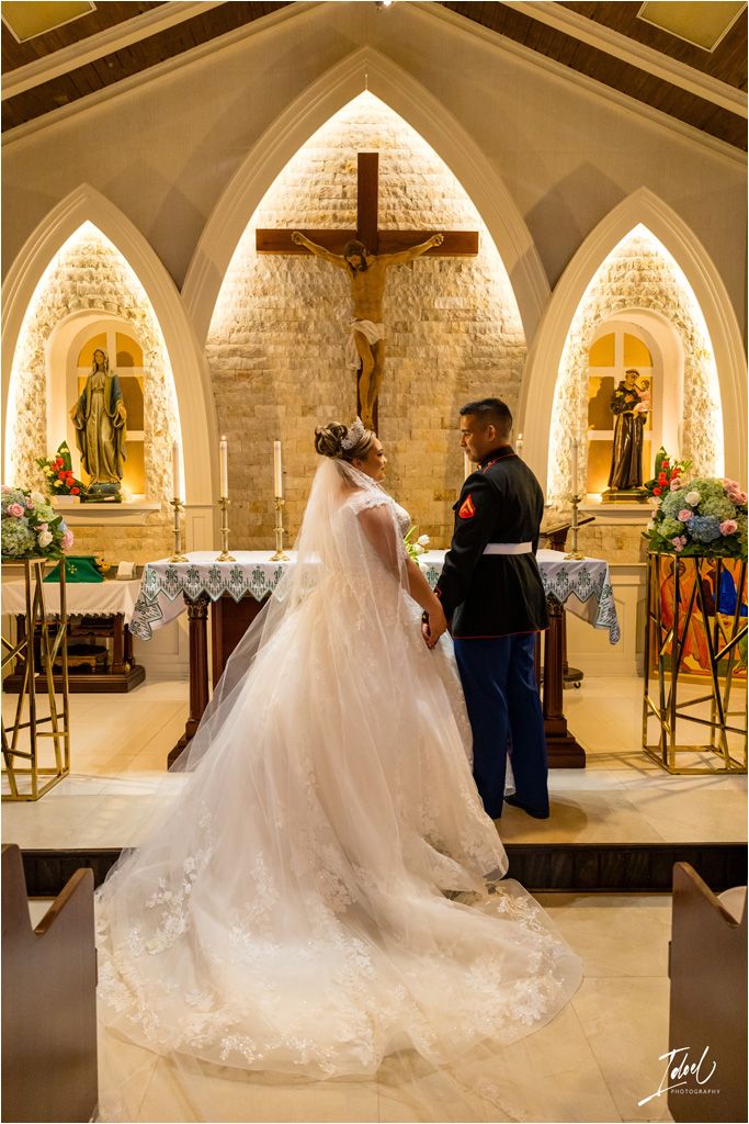 A couple stands at a church altar with gothic arches and religious statues illuminated in warm light during their wedding ceremony.