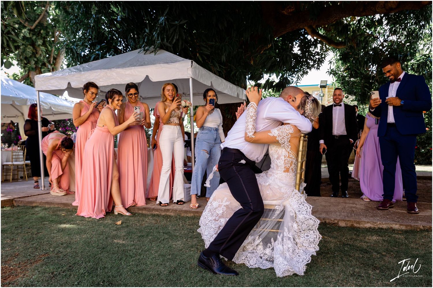Wedding couple performs a dip move on an outdoor dance floor surrounded by bridesmaids in pink gowns.