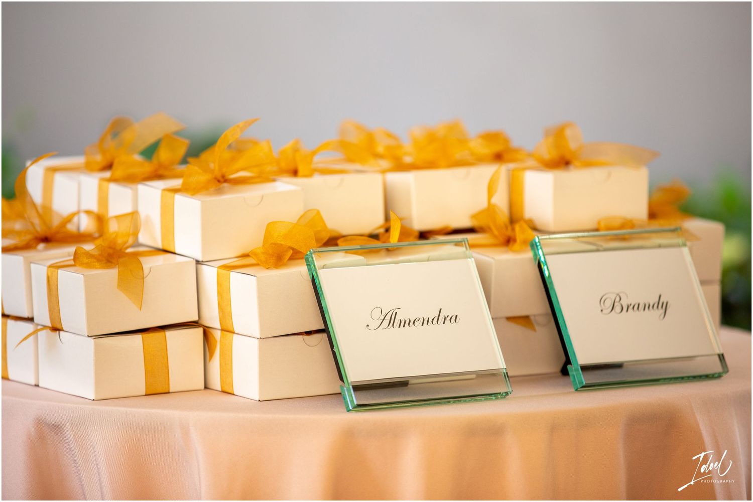 Elegant white wedding favor boxes decorated with golden orange ribbon and name cards arranged on a table.