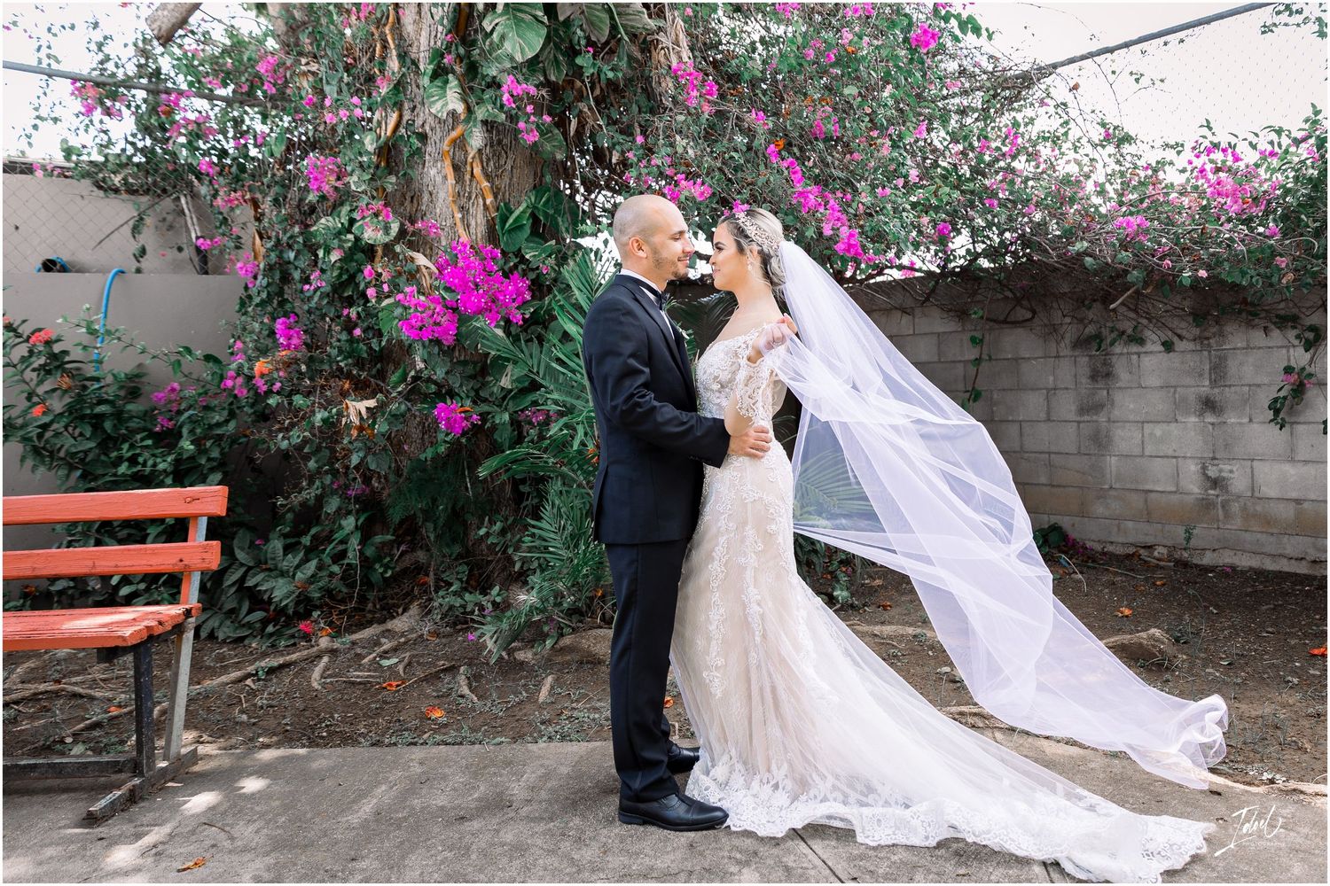 Romantic garden wedding scene with flowing veil and purple bougainvillea backdrop.