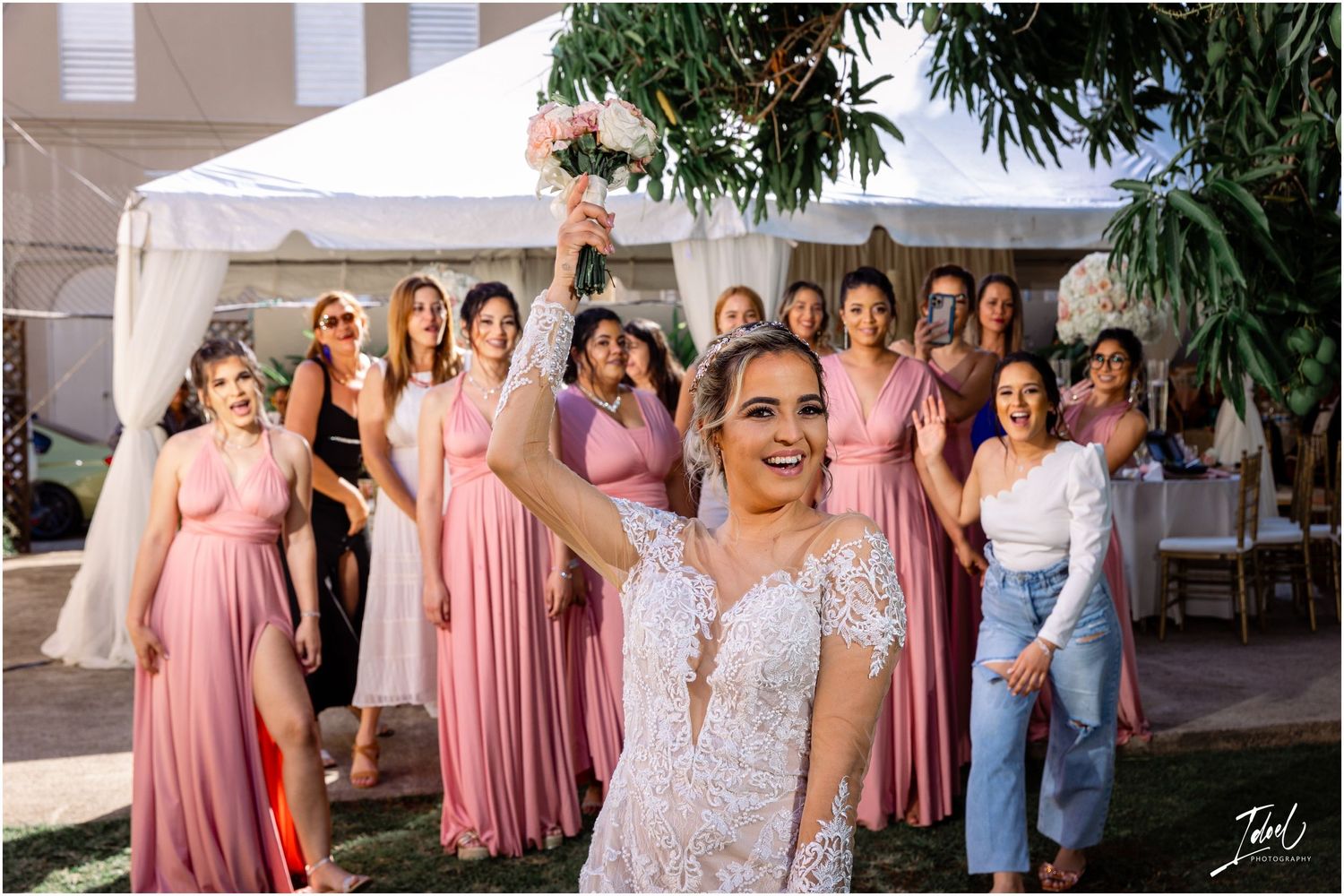 Celebratory wedding party photo with bridesmaids in pink dresses gathered around.