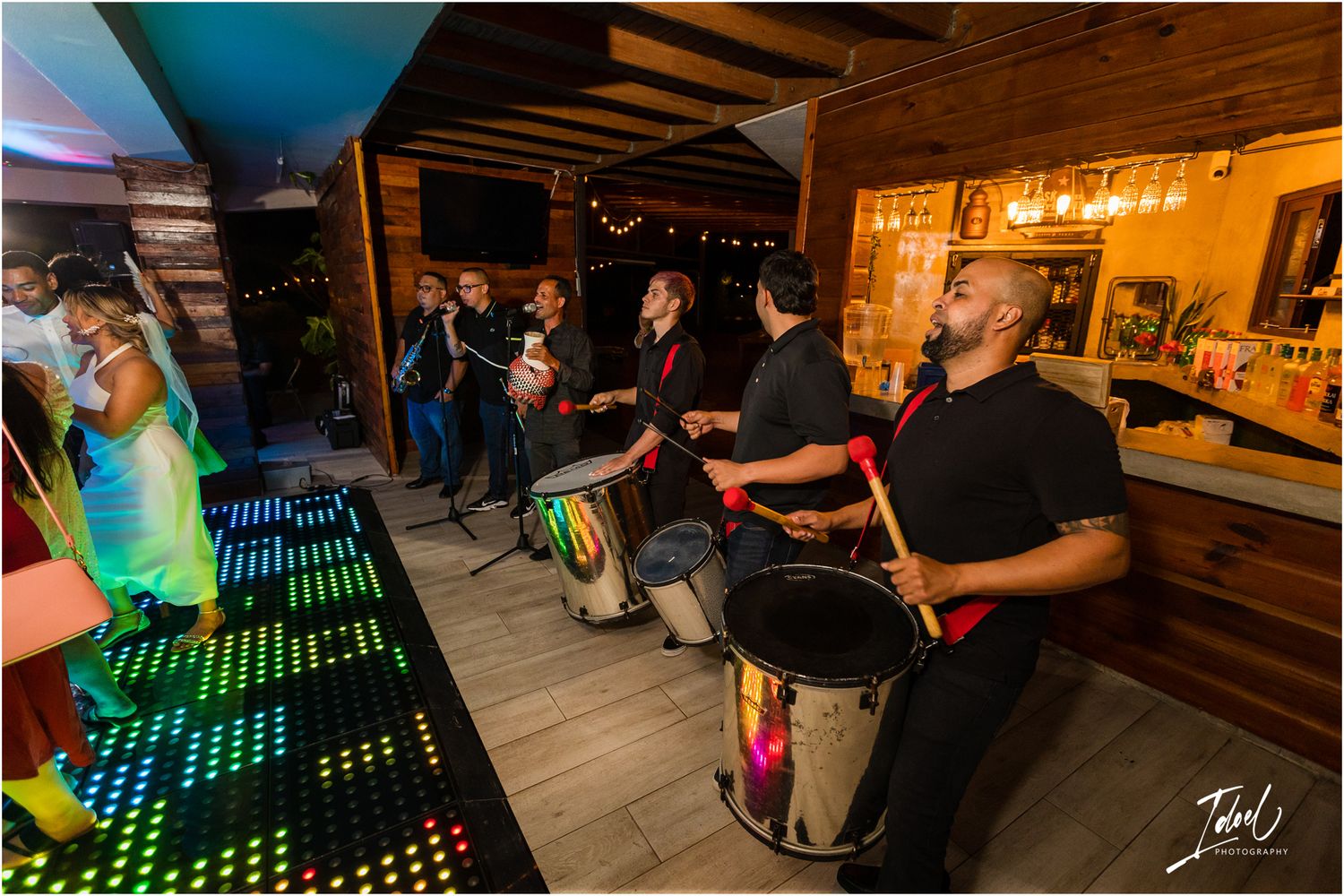 Drummers performing at a lively wedding reception with colorful lighting and bar setup.
