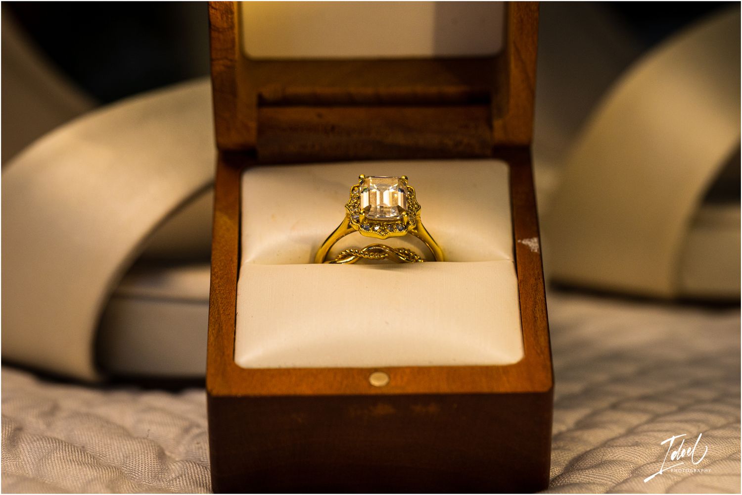 A sparkling diamond engagement ring displayed in a brown wooden jewelry box.