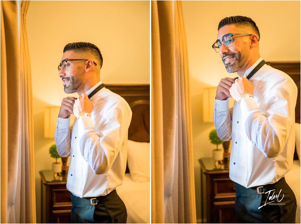 Person wearing blue glasses and white dress shirt adjusts their tie in front of a mirror with warm lighting.