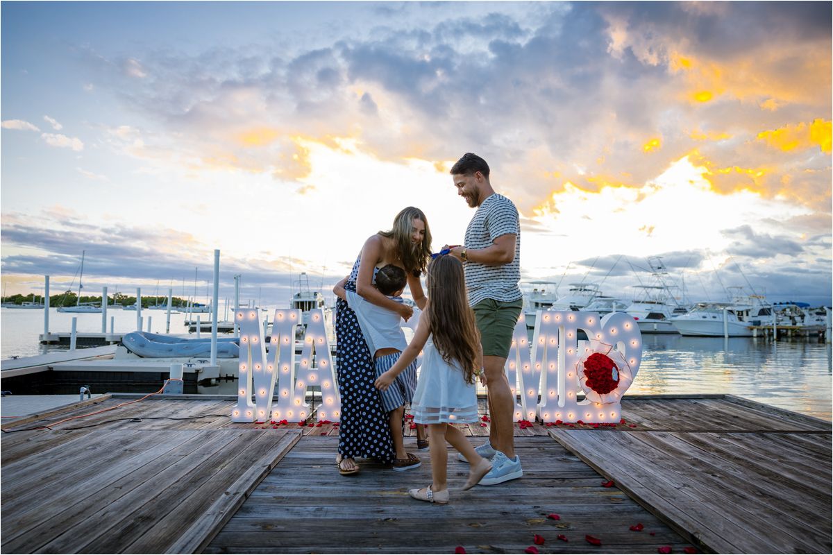 A special moment captured at sunset on a wooden dock with illuminated letters and boats at marina.
