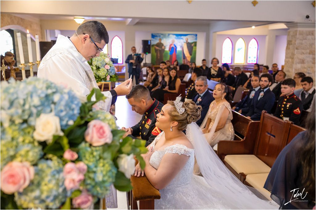 Wedding mass in a church with clergy presiding over the ceremony and guests seated in wooden pews.