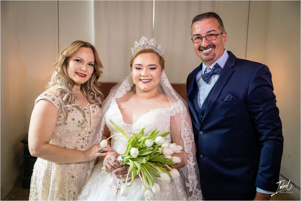 Three people pose together at a wedding celebration with white tulip bouquet.