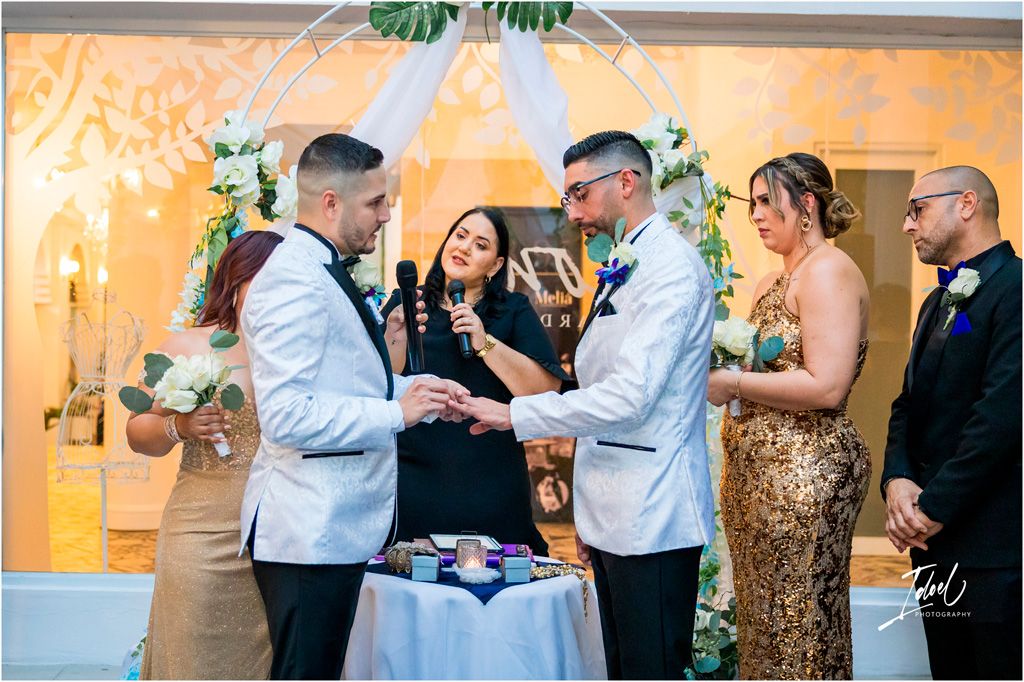 Two people exchanging rings during wedding ceremony as guests watch and officiant leads the service.