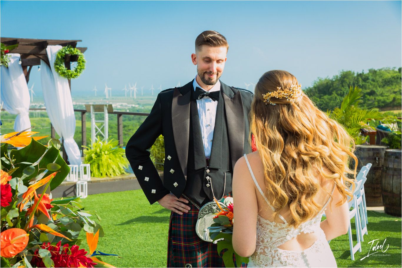 Couple in wedding attire sharing a moment at outdoor venue with tropical backdrop.