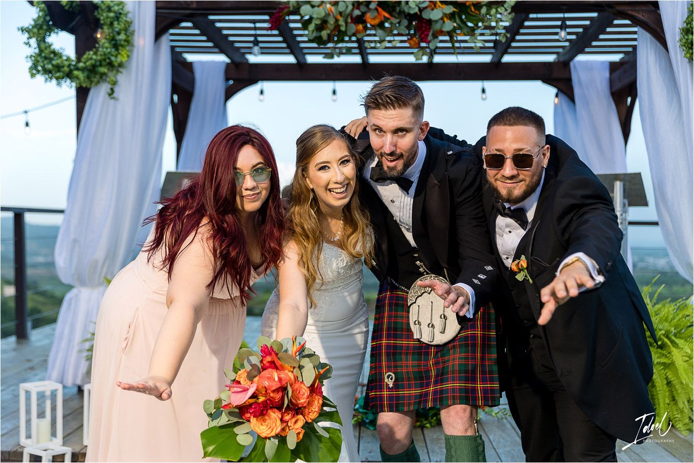 Wedding party shares candid laughing moment under decorated outdoor pergola.