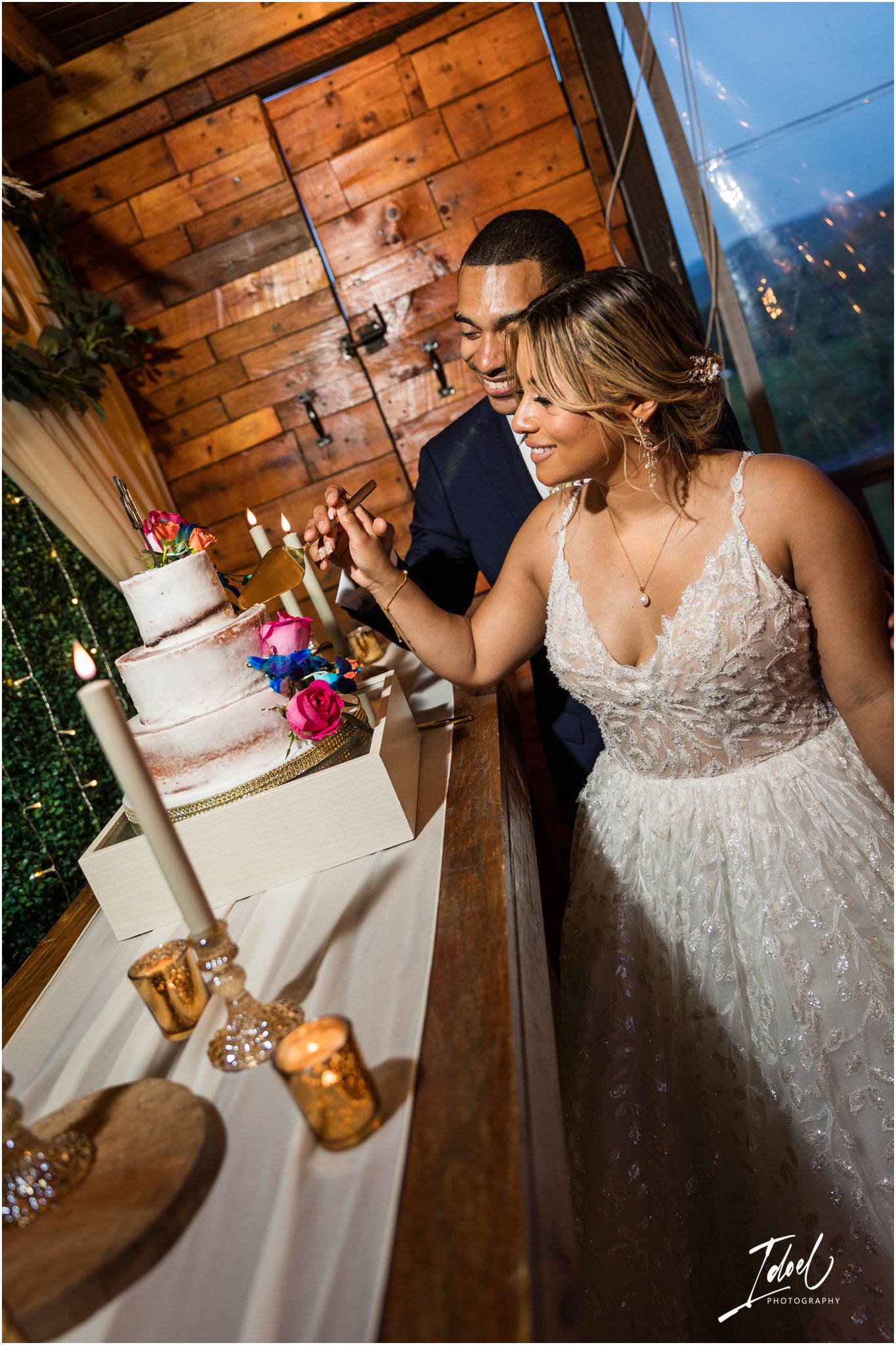 A wedding couple admires their three-tiered white cake decorated with colorful flowers.