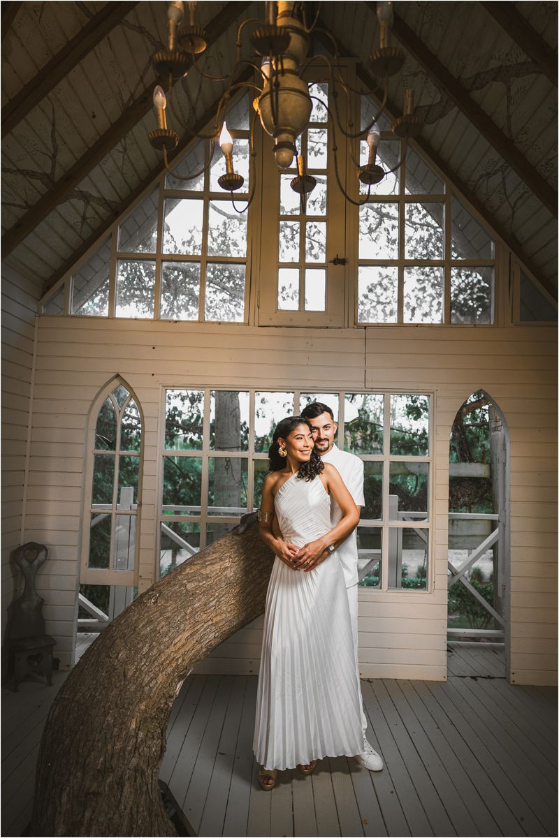 Two brides share an intimate moment in a rustic chapel with gothic windows and wooden floors.