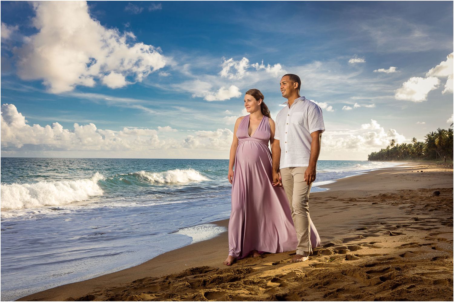 Couple walks along tropical beach shoreline at sunset in romantic beach photoshoot.