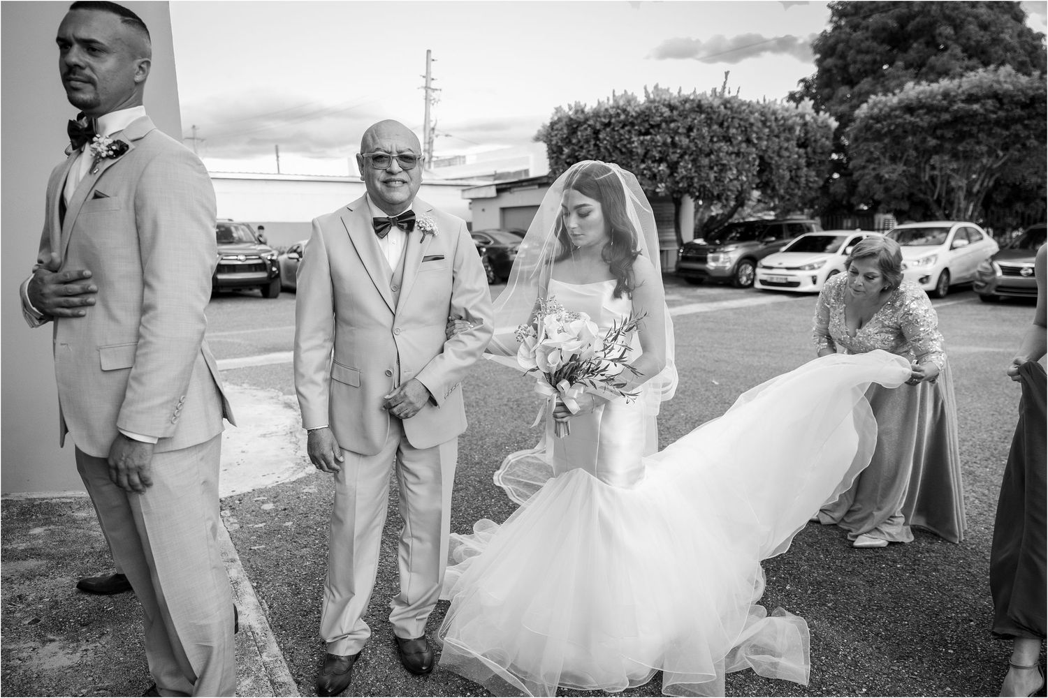 A joyful wedding party walks together outdoors in black and white formal attire on a sunny day.