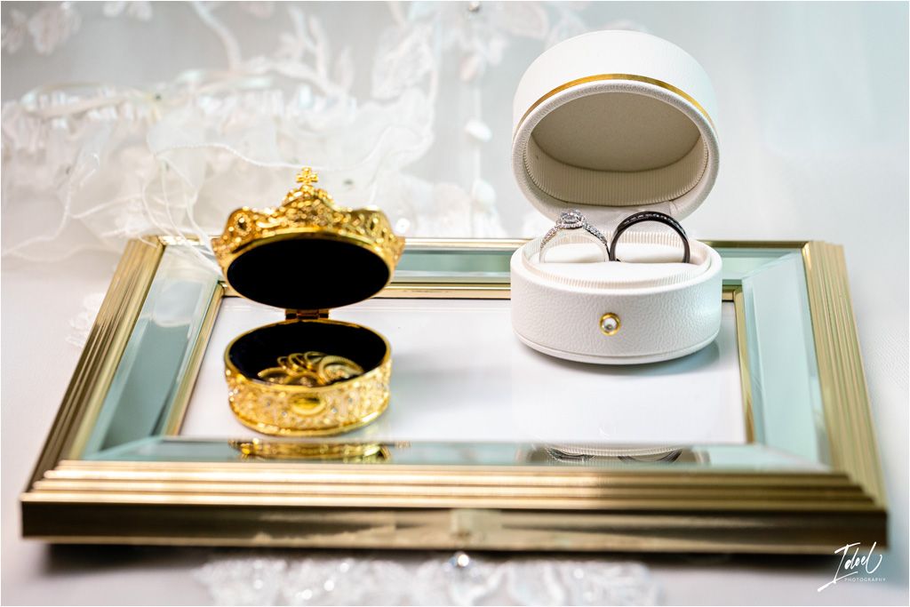 Wedding rings displayed in ornate white and gold boxes on a mirrored tray.