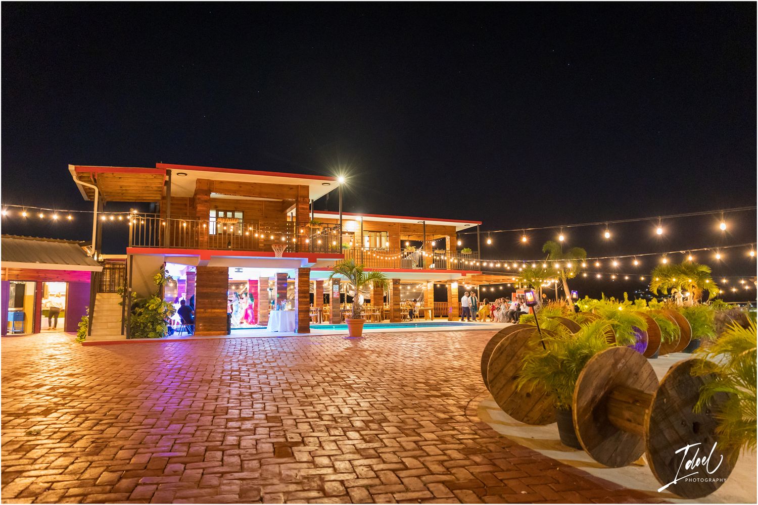 Nighttime view of an illuminated outdoor shopping plaza with string lights and brick pavement.
