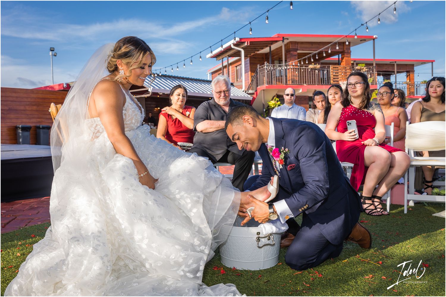 A wedding ceremony guest participates in a festive shoe game tradition on an outdoor patio.