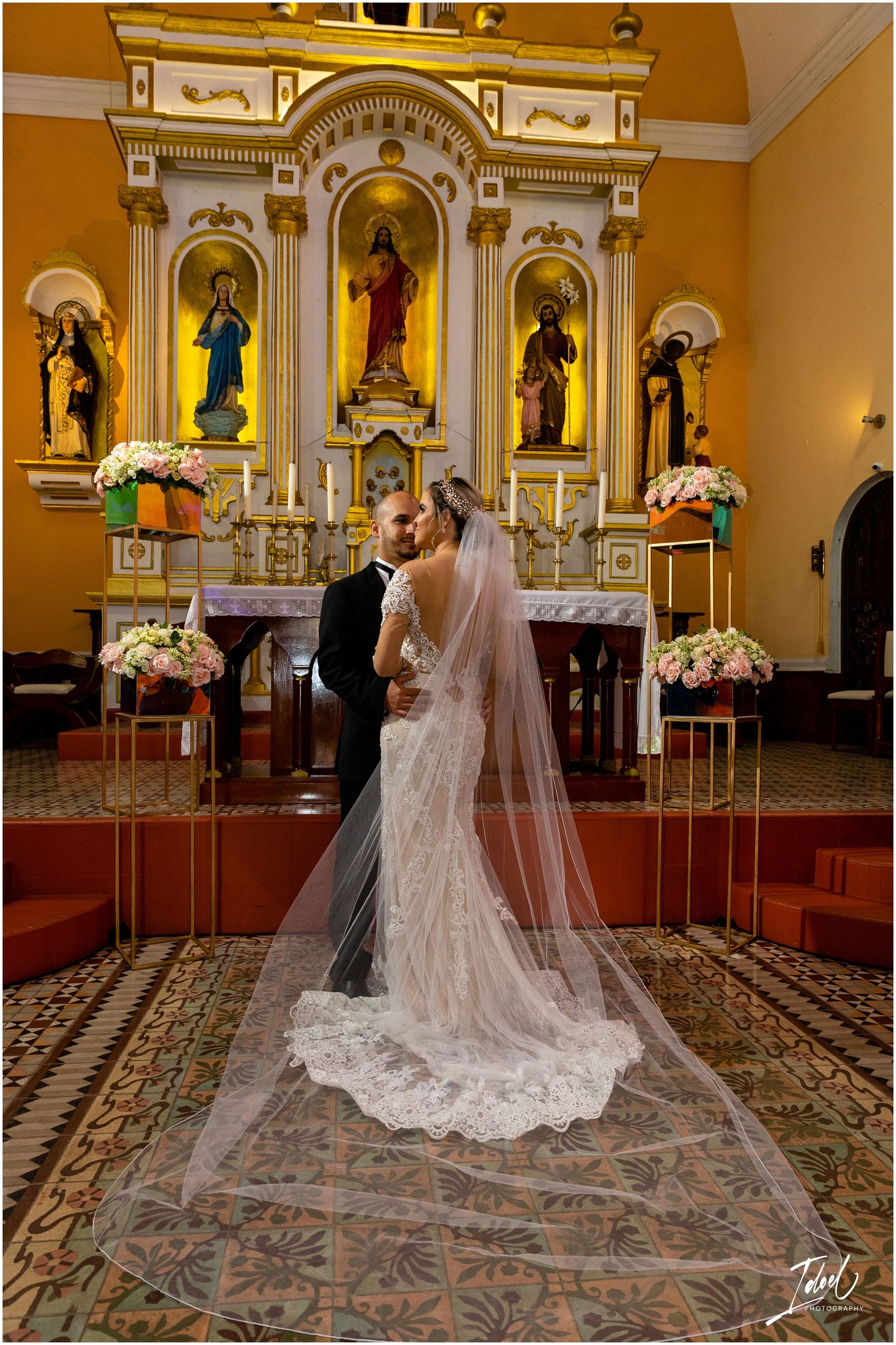 Newlyweds share intimate moment before ornate church altar with long flowing veil.